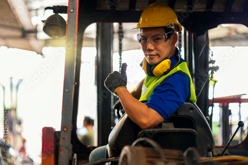 Engineer or technician Concept. A male employee driving a forklift and showing thumb up in factory. photo