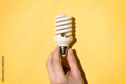 Male hand holding a light bulb on a yellow background, top view. Burnt out light bulb, flat lay