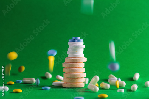 Stacks of pills of various sizes and colors on a green background, falling down and scattered pills. Medical concept of thoughtless, non-prescription and unregulated drug use