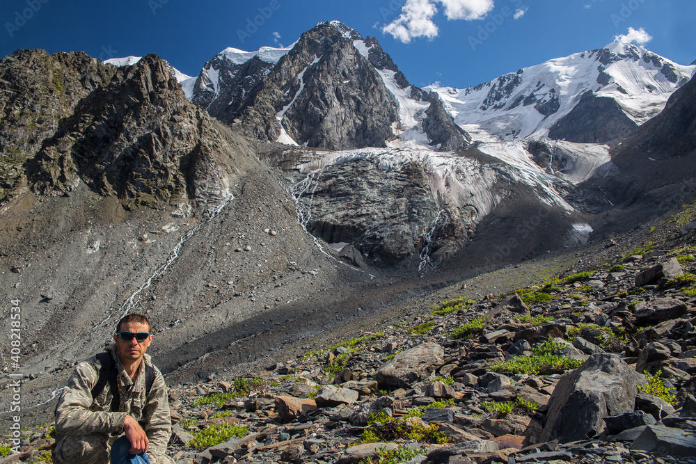 Male traveler on the background of high snow-capped mountains.
