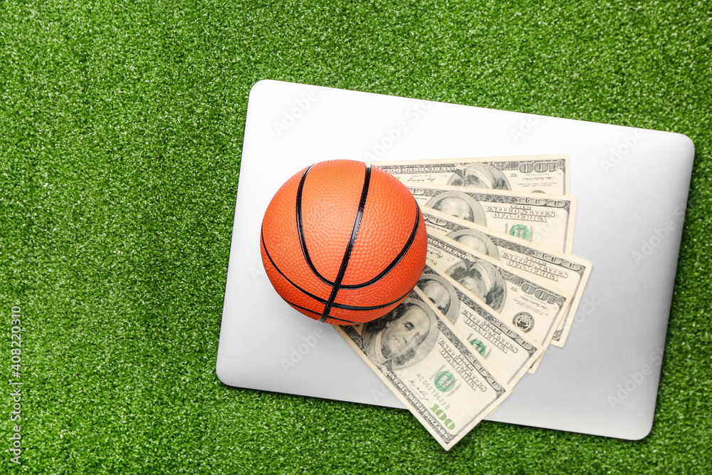 Obraz premium Money, laptop and ball for playing basketball on color background. Concept of sports bet