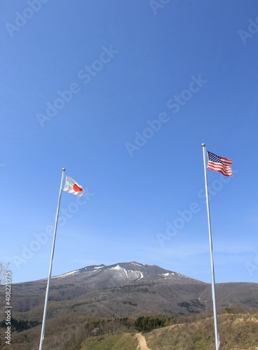 日米の国旗の間に、うっすらと雪を被った山がある風景