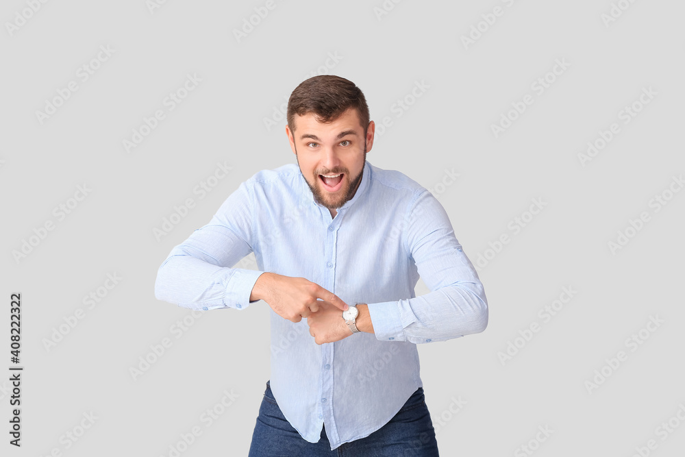 Handsome man pointing at wristwatch on light background Handsome man pointing at wristwatch on light background