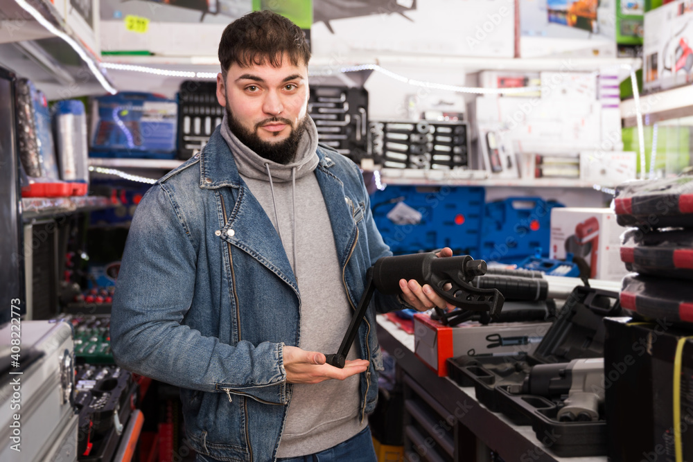Young man hardware store visitor selects electric tool