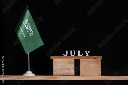 Wooden calendar of July with Saudi Arabia flag on black background. Dates of Saudi Arabia in July