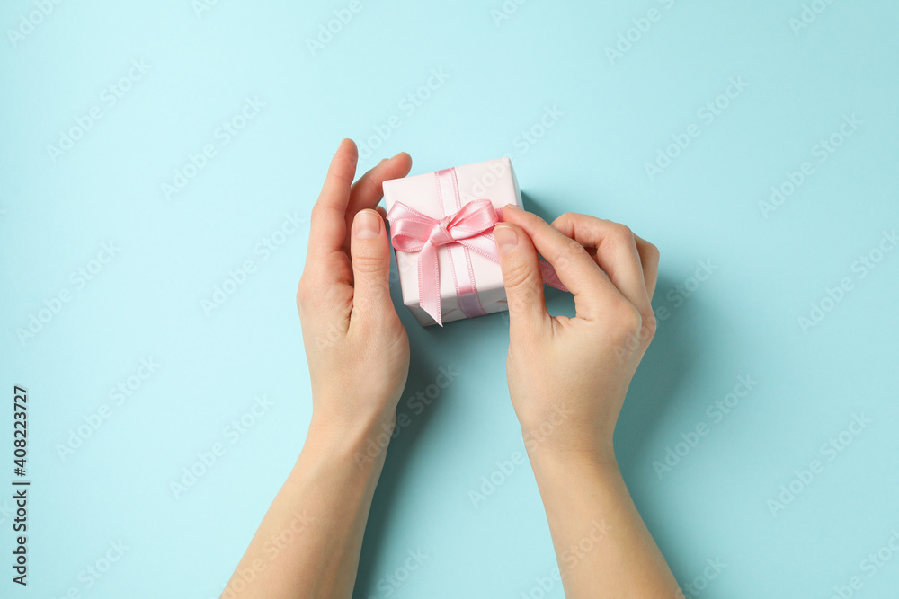 Female hands holding gift box with pink ribbon on blue background Female hands holding gift box with pink ribbon on blue background