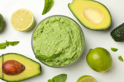 Bowl of guacamole, avocado, lime and basil on white background, top view