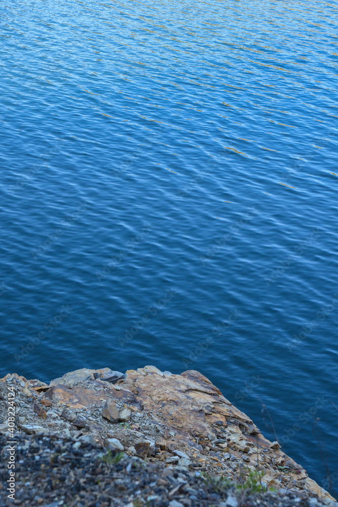 Stone rocks near water, on the background of lake, river, sea, ocean. Blue clear water. Artificial reservoirs