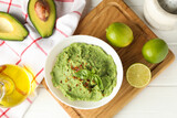 Concept of tasty eating with guacamole and ingredients on white wooden background
