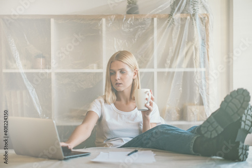 Freelancer lifestyle. Home startup. Lockdown creative distance work. Relaxed woman enjoying coffee break with laptop at light remote office covered with polyethylene film. photo