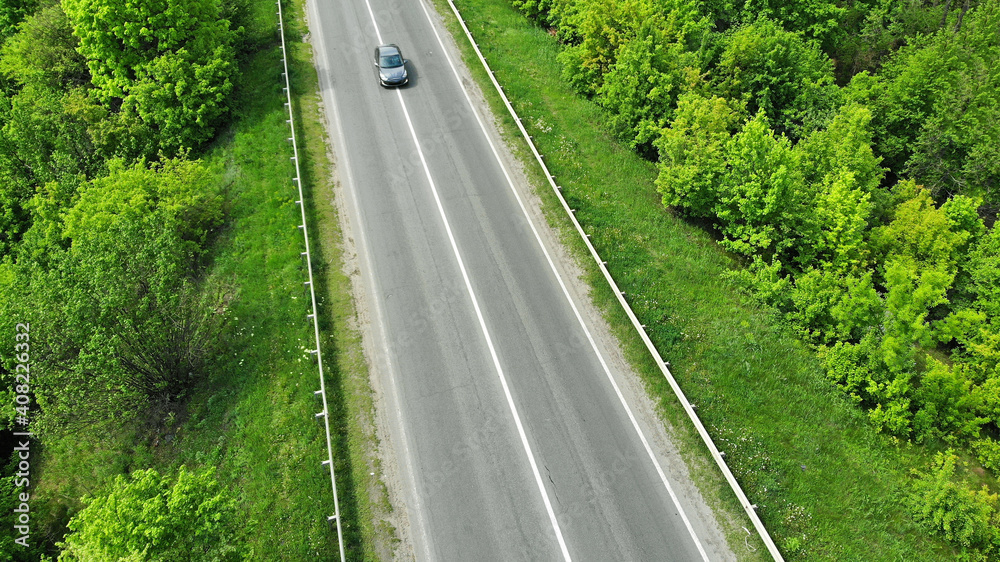 Aerial. Highway asphalt road between green trees. One car alone. View above from drone.