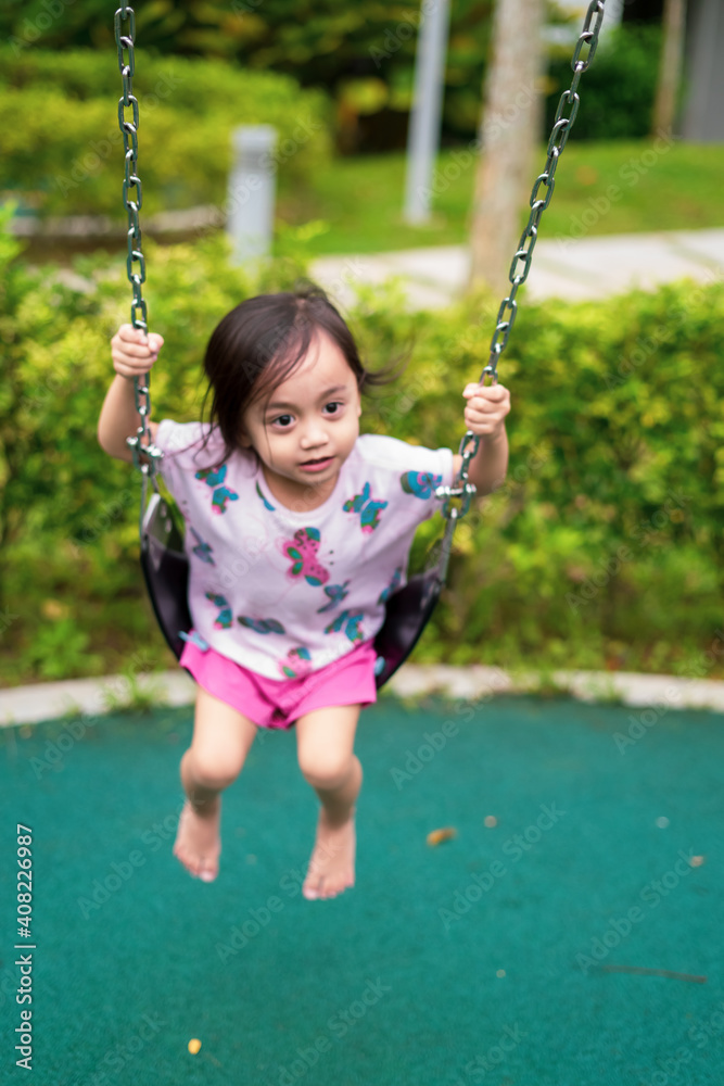 Blurry image of cute small child smiling while playing swing by herself at the kid's playground, view of blurry kid sitting on swing alone.