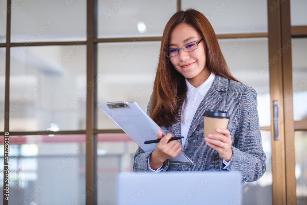 Closeup image of a beautiful young asian business woman drinking coffee and using laptop computer while working in office