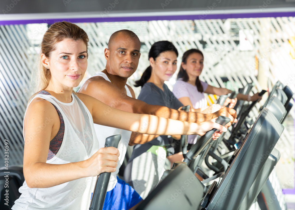 Fototapeta premium People having running elliptical trainer class in health club