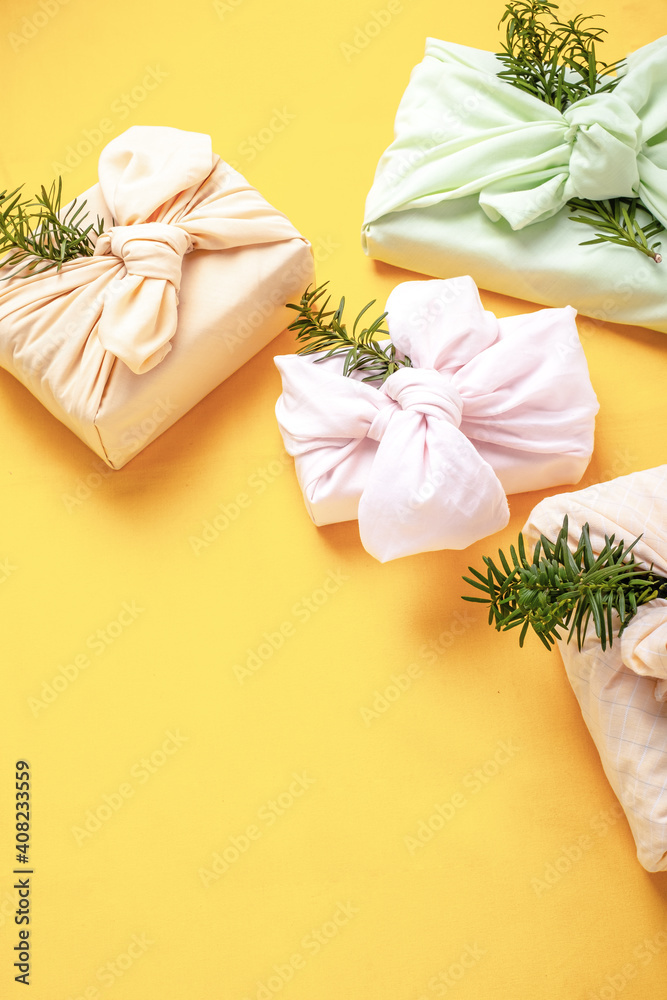 Fabric wrapped gifts with branches on a yellow background. Reusable sustainable gift wrapping alternative zero waste concept.