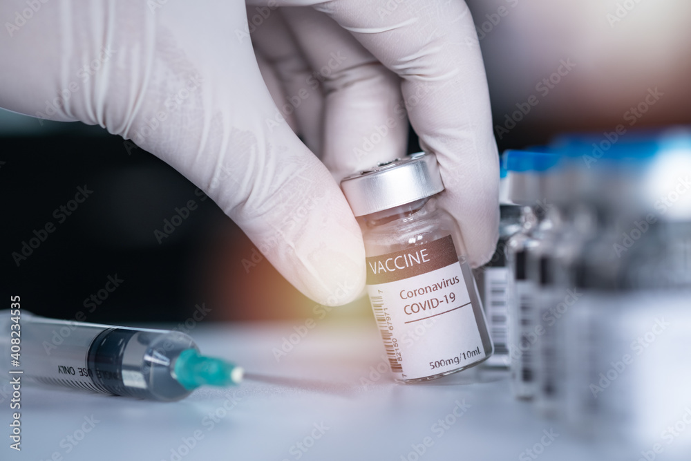 Hand wearing a medical nitrile surgical glove and pick or hold a bottle of covid19 vaccine. Vaccination, immunization, treatment to cure Covid 19 Corona Virus infection Concept Hand wearing a medical nitrile surgical glove and pick or hold a bottle of covid19 vaccine. Vaccination, immunization, treatment to cure Covid 19 Corona Virus infection Concept