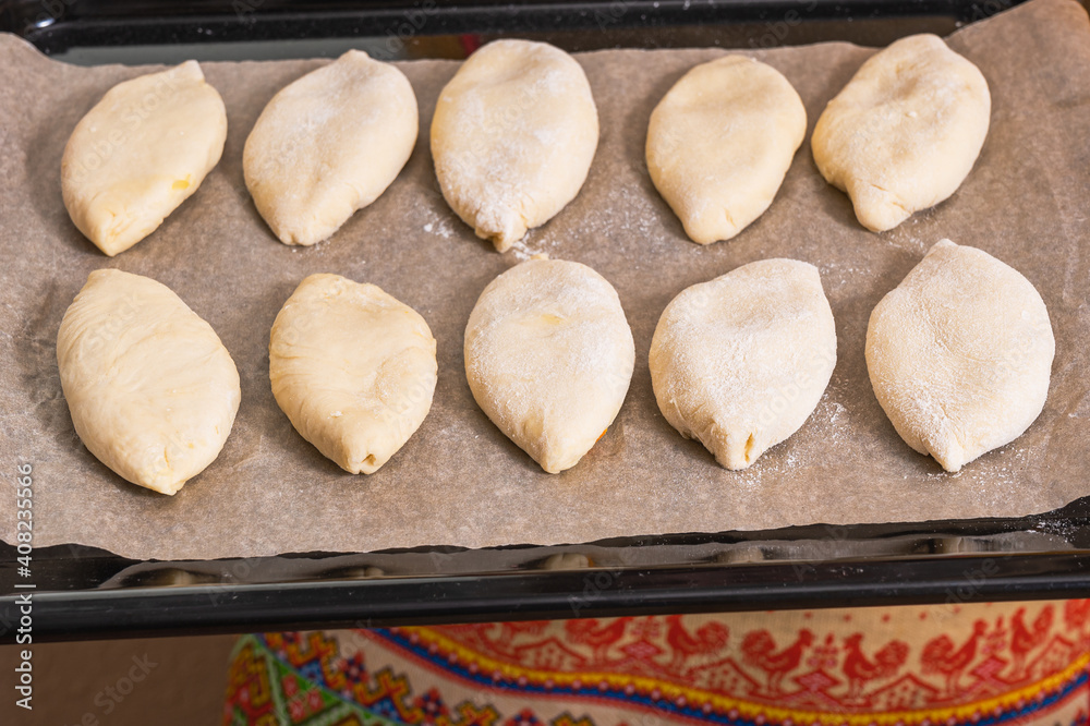 On a baking sheet are raw Russian dough pies with filling. Homemade baking