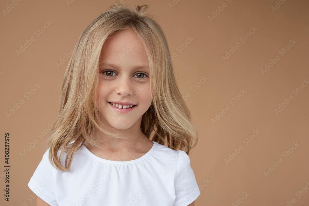 Closeup front portrait of pretty little girl with wavy blond hair, dressed in white shirt, over beige background. Closeup front portrait of pretty little girl with wavy blond hair, dressed in white shirt, over beige background.