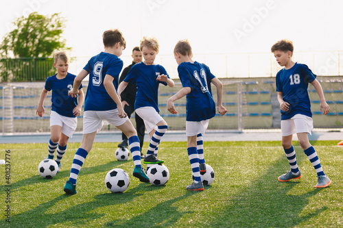 Group of children playing soccer on training session. Kids in football club wearing blue jersey shirts and soccer kits. Happy boys practicing football with coach on a sunny day