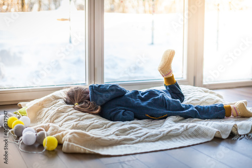 Boring little girl lying on a woolen blanket near the window