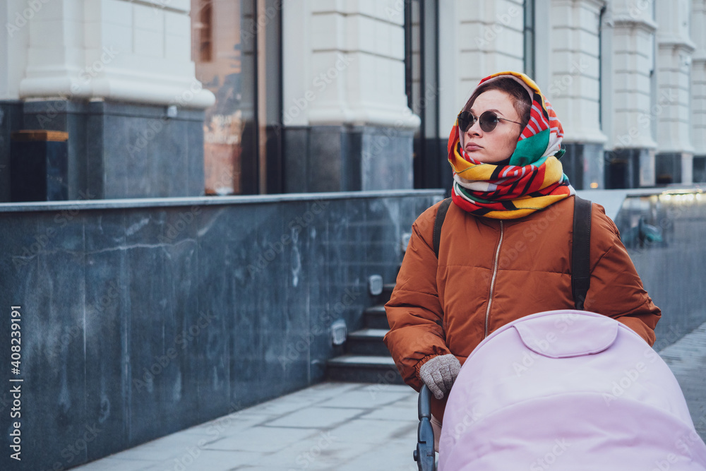 Obraz premium Fashionable modern mom with a stroller on a walk in the city, autumn. Mom drives a stroller through the streets, close-up