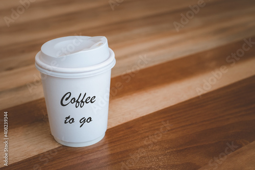 Takeaway hot coffee cup in white color with text coffee to go for take away. Paper coffee cup on wooden table in the cafe or coffee shop.