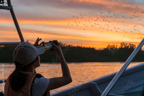 A woman takes a photo with her phone during a sunset boat tour in Pasir Penambang, Malaysia. The main attractions of this area are the Sky Mirror, Firefly watching and eagle feedings.