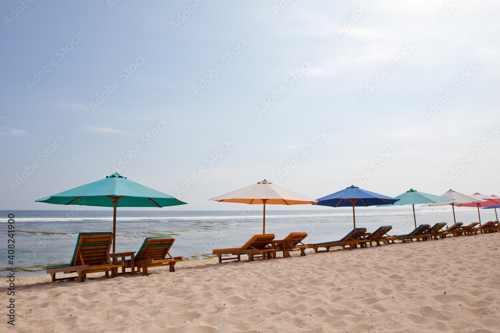 Fototapeta premium Beach for tourists. Sun loungers and umbrellas on the white sand. Bali island resort, Indonesia.