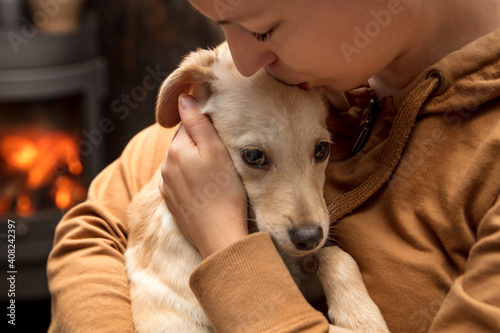 Woman is kissing and cuddling her cute puppy dog in her arms