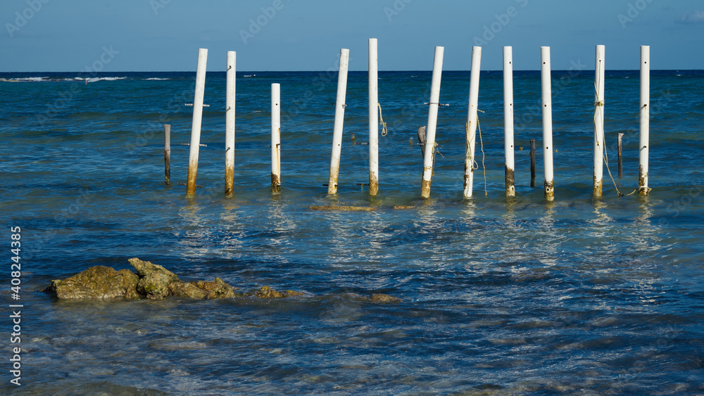 White poles driven into the blue sea water in Bacalar, Mexico