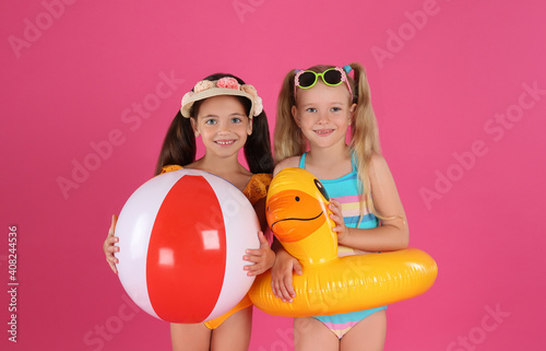 Cute little children in beachwear with bright inflatable toys on pink background