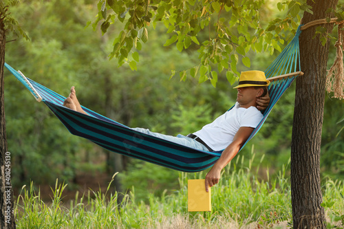 Man with book resting in comfortable hammock at green garden