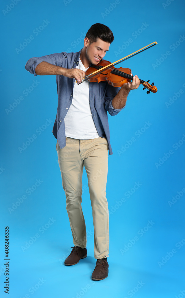 Fototapeta premium Happy man playing violin on light blue background