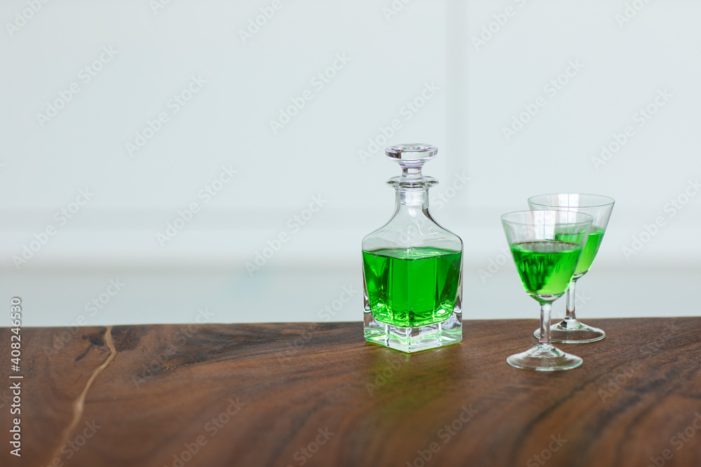 A green poisonous drink in a small bottle and two cocktail glasses on a table. A strong venomous chemical mixture.