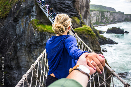 Lovely couple holding hands and walking on the Carrick-a-rede rope bridge in Northern Ireland photo