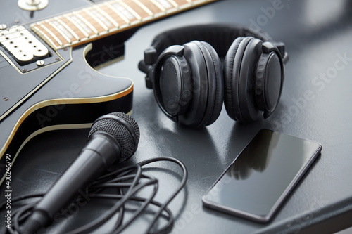 leisure, music and musical instruments concept - close up of bass guitar, smartphone, microphone and headphones on black table