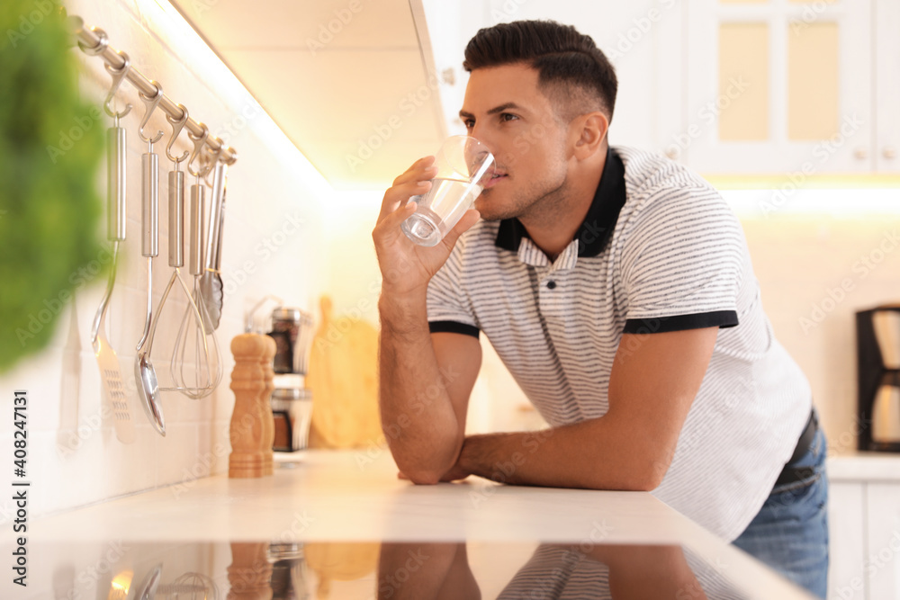 Man drinking glass of pure water at countertop in kitchen Man drinking glass of pure water at countertop in kitchen