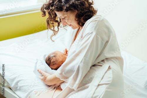 Brunette curly mother with her newborn baby boy at the hospital a day after a cesarean section birth labor. Breast feeding, a new born sucking mother breast. photo