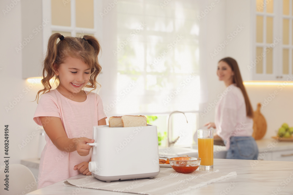 Cute little girl using toaster at table in kitchen Cute little girl using toaster at table in kitchen