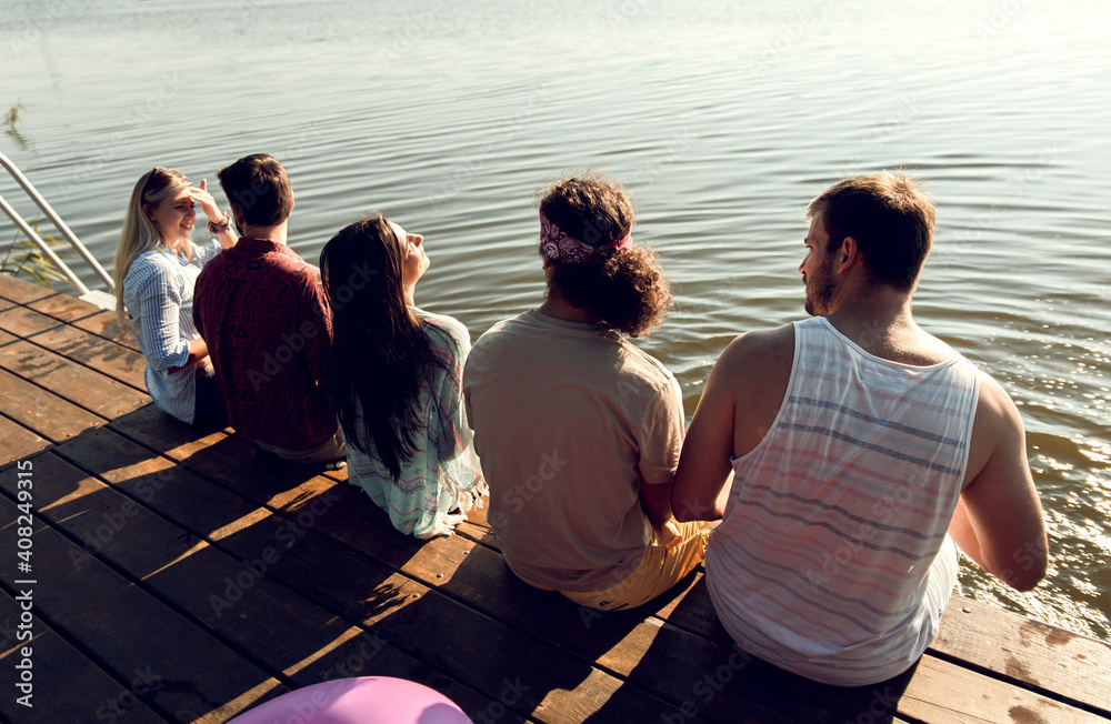 © Zoran Zeremski - Group of friends sitting on the edge of a pier having fun and enjoying a summer day at the lake.
