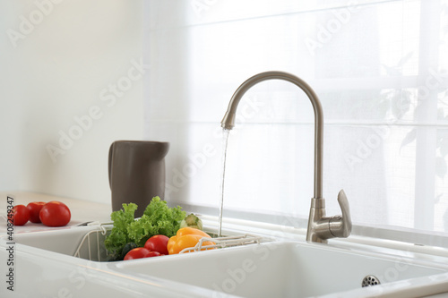 Many fresh ripe vegetables under tap water in kitchen sink