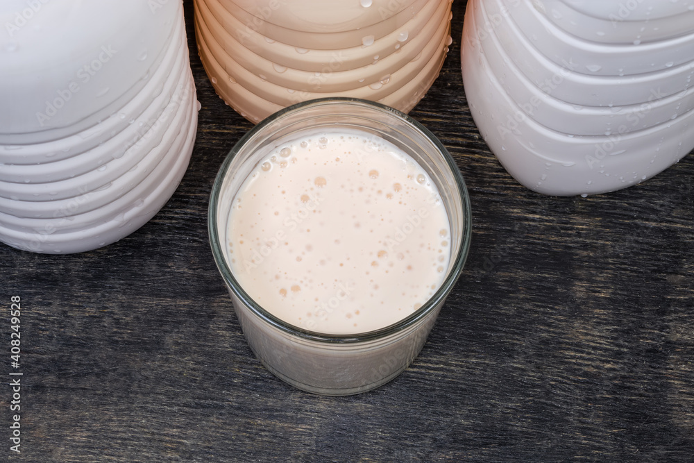 Glass of fermented milk drink against plastic bottles, top view