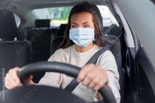 safety and people concept - young woman or female driver in medical mask driving car in city