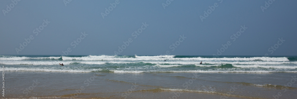 Cornwall people having fun in the waves and sea in wetsuits with surf boards at Porthtowan Cornish north coast