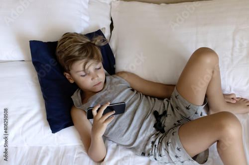 Above view of a kid using cell phone while relaxing on a bed.
