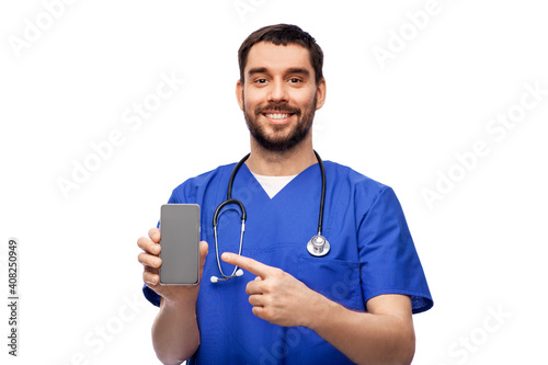 medicine, healthcare and technology concept - happy smiling doctor or male nurse in blue uniform with smartphone and stethoscope over white background