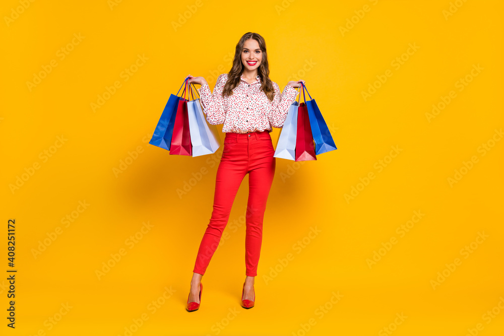 Full size photo of adorable lady standing hands hold bags toothy smile isolated on yellow color background Full size photo of adorable lady standing hands hold bags toothy smile isolated on yellow color background
