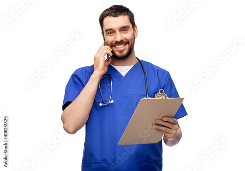 healthcare, profession and medicine concept - happy smiling doctor or male nurse in blue uniform with stethoscope and clipboard calling on smartphone over white background © Syda Productions