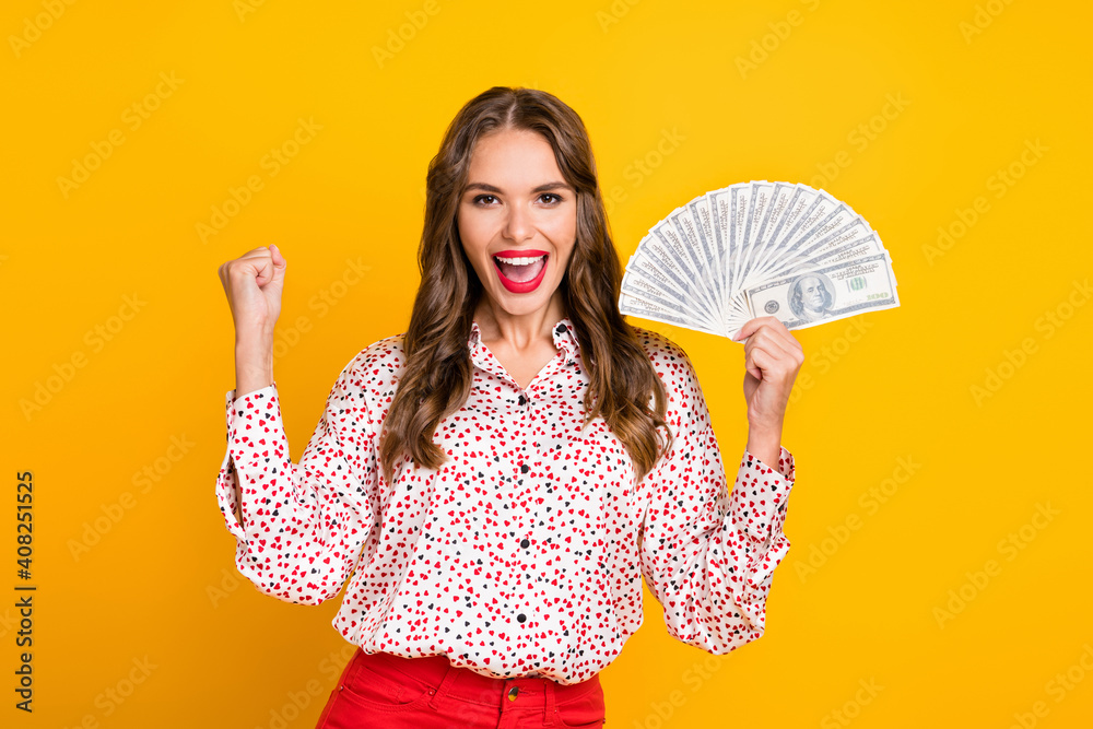 Photo of excited cheerful girl hold fan cash open mouth raise fist wear heart print shirt isolated yellow color background