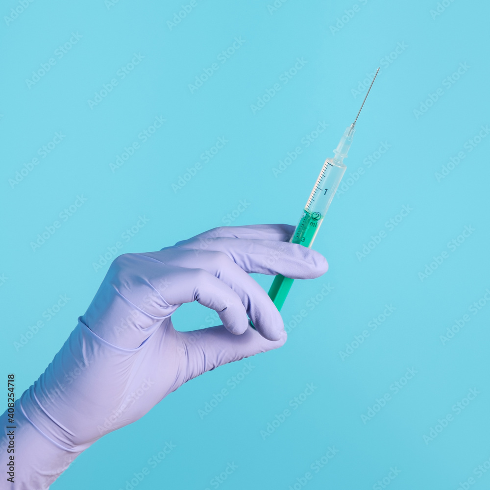 Syringe for injection in hand, latex medical gloves on hand. On a blue background. Syringe for injection in hand, latex medical gloves on hand. On a blue background.